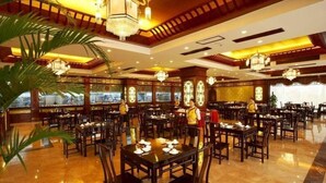 Un restaurant spacieux, doté de nombreuses tables et chaises, de grandes fenêtres et d’un éclairage décoratif.