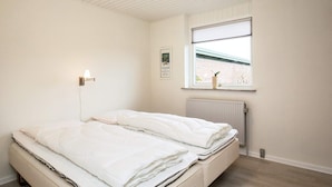 A bedroom with a bed, a window with blinds, a wall-mounted light, and a radiator. - 6 Person Holiday Home in Pandrup (Pandrup)