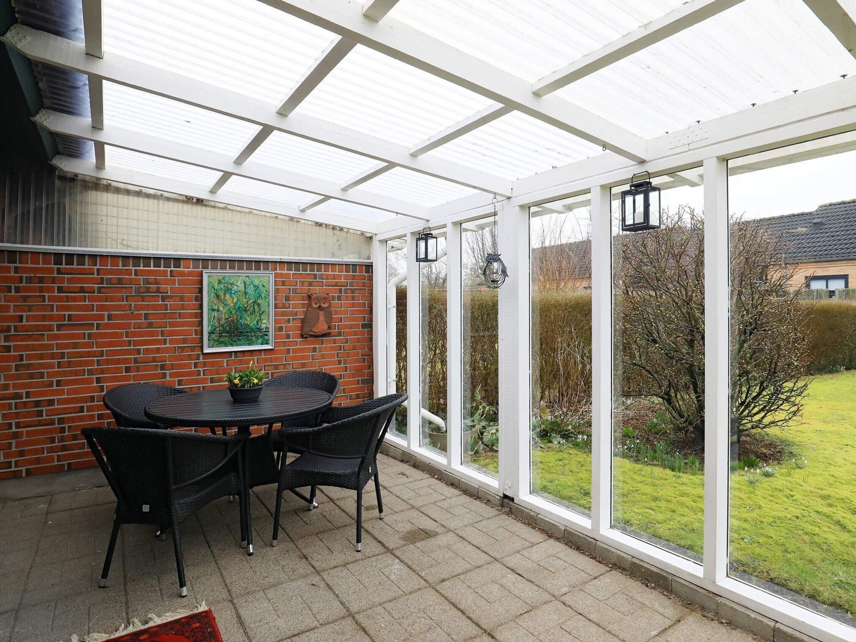 A covered patio with a brick wall, a table with chairs, and a view of a garden.
