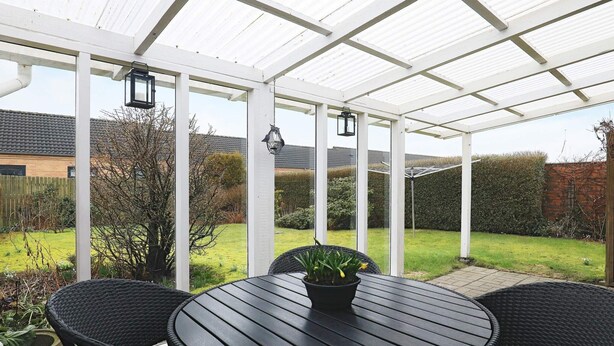 A covered patio area with a round table and four chairs, a potted plant, and a lantern. - 6 Person Holiday Home in Pandrup (Pandrup)