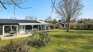 A house with a covered patio, a lawn, and a tree. - 4 Person Holiday Home in Jaegerspris (Jægerspris)