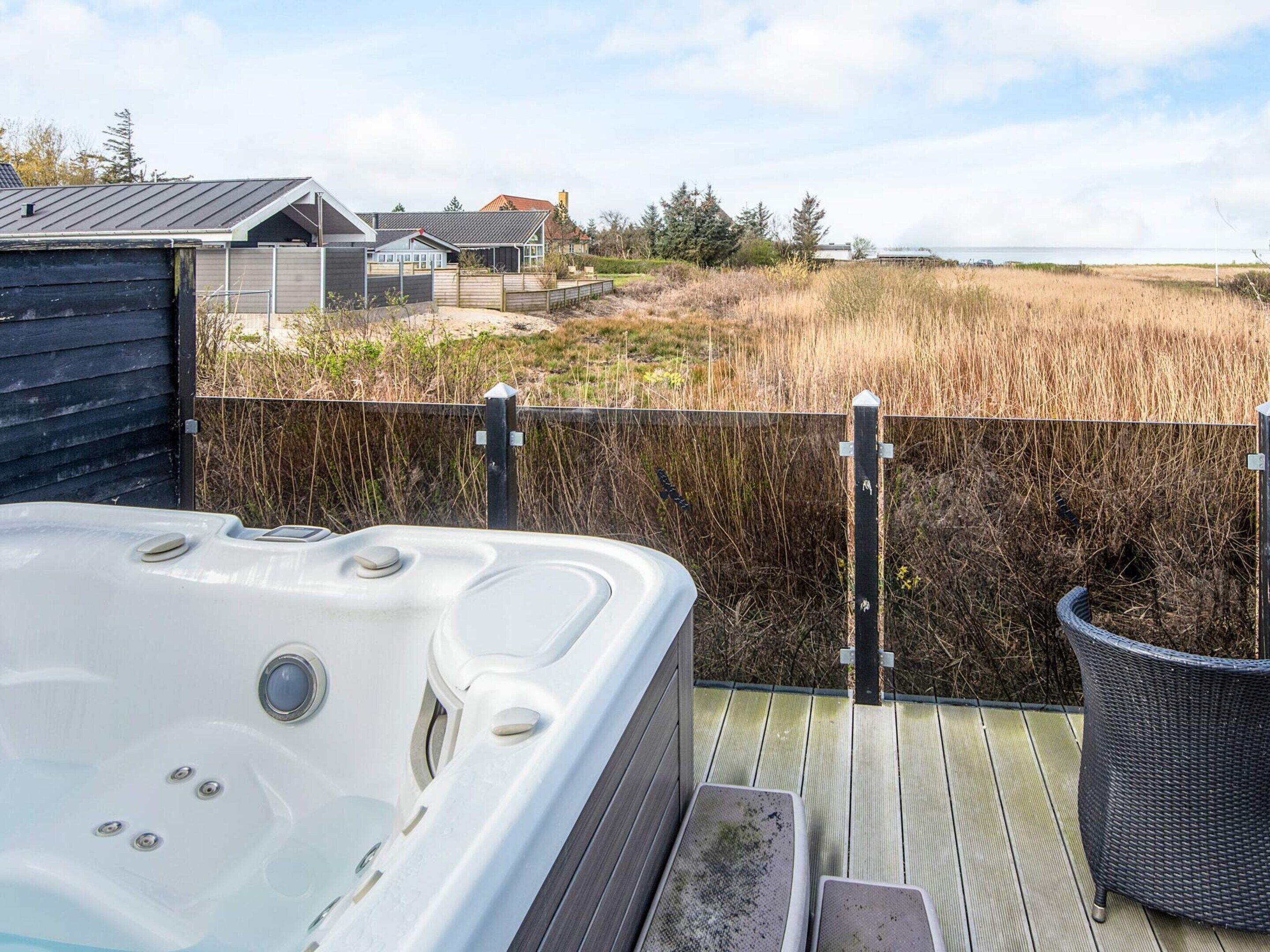 Ein Whirlpool auf einer Holzterrasse mit Blick auf einen Strand und Häuser im Hintergrund.