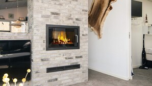 Ein modernes Wohnzimmer mit Kamin aus Stein, einem aufgehängten Tierfell und einem großen Flachbildfernseher.