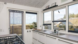 Eine moderne Küche mit Gasherd, weißen Schränken, einem großen Fenster und Blick ins Freie.