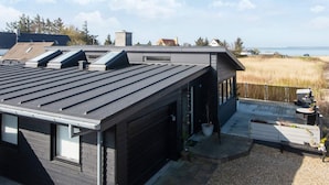Ein modernes Haus mit Flachdach, Dachfenstern und einer Terrasse mit Blick auf einen Strand.