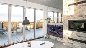 Ein modernes Wohnzimmer mit einem großen Glasschreinzugang zu einer Terrasse, einem Kamin und einem runden Couchtisch mit Fernbedienung.