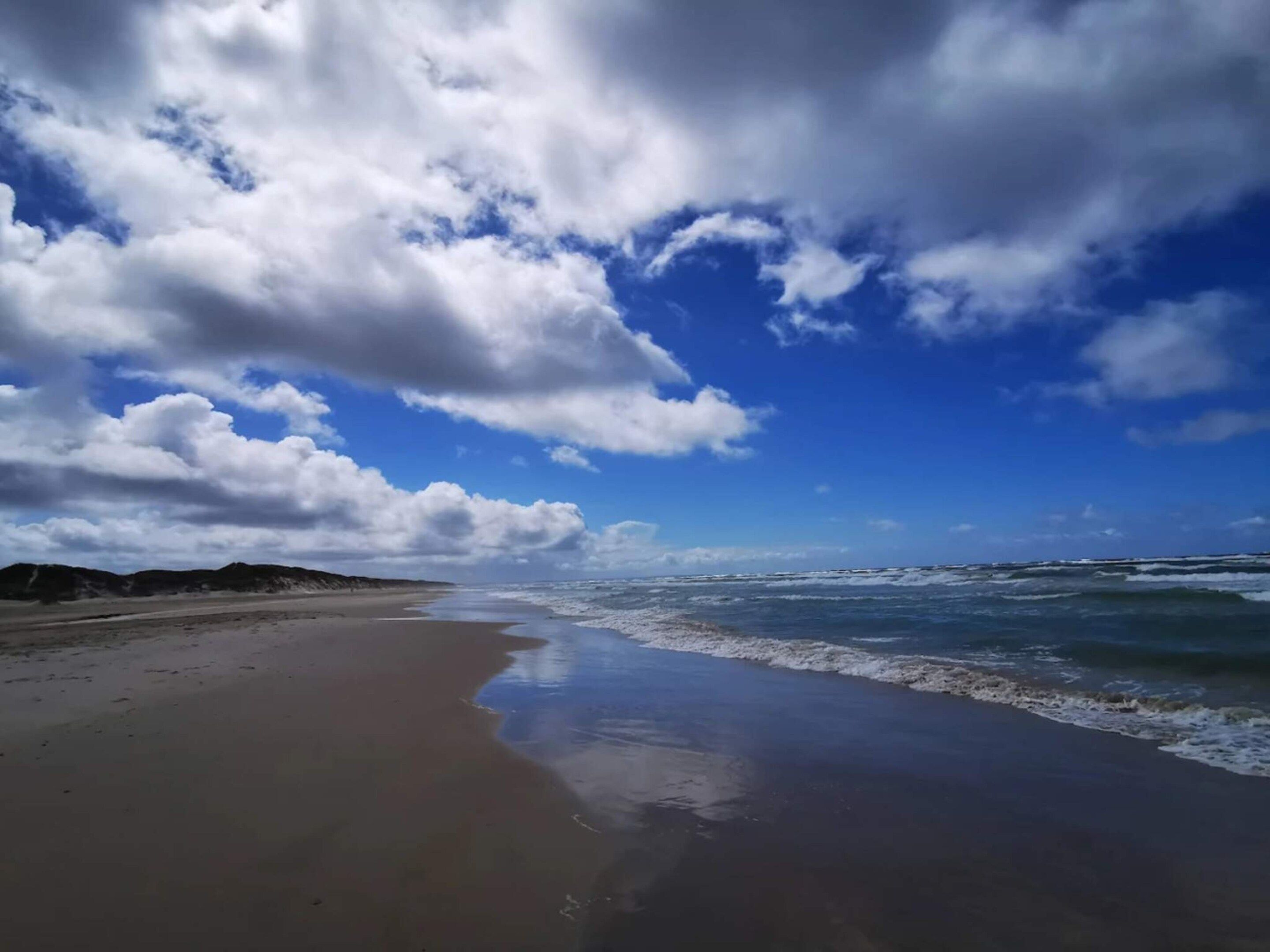 A beach with a wide sandy shore and waves approaching the beach.