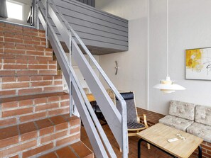 Una escalera con barandilla de metal conduce a una zona superior, donde hay un sofá, una mesa y una lámpara fijada a la pared.