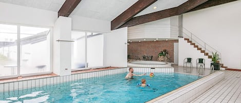 An indoor swimming pool with a tiled floor, a staircase, and a view of the outside.