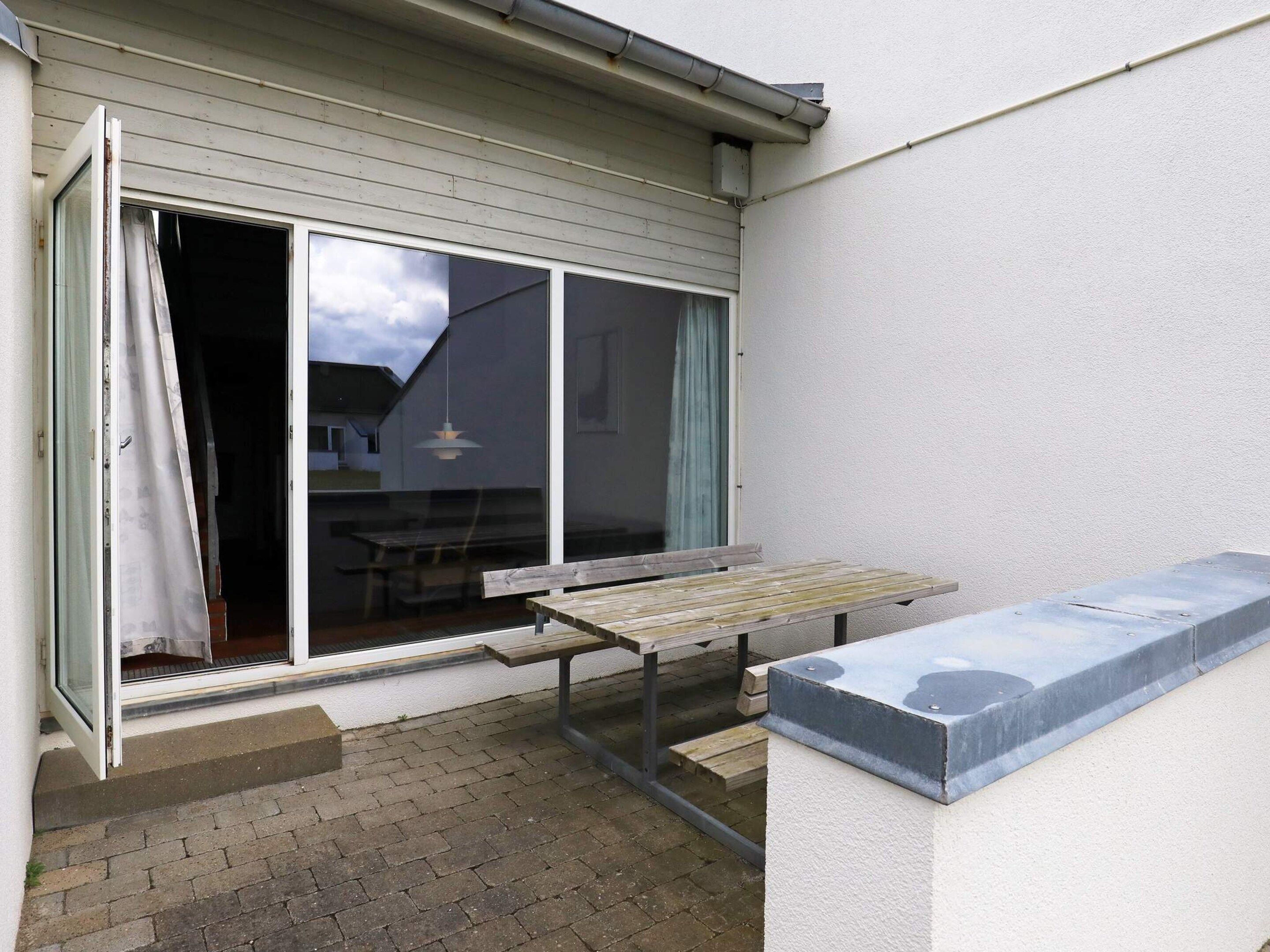 A patio area with a wooden bench, a table, and a sliding glass door leading to an interior space.