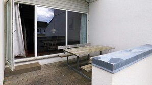 Un espace patio aménagé avec un banc en bois, une table et une porte-fenêtre coulissante donnant sur un espace intérieur.