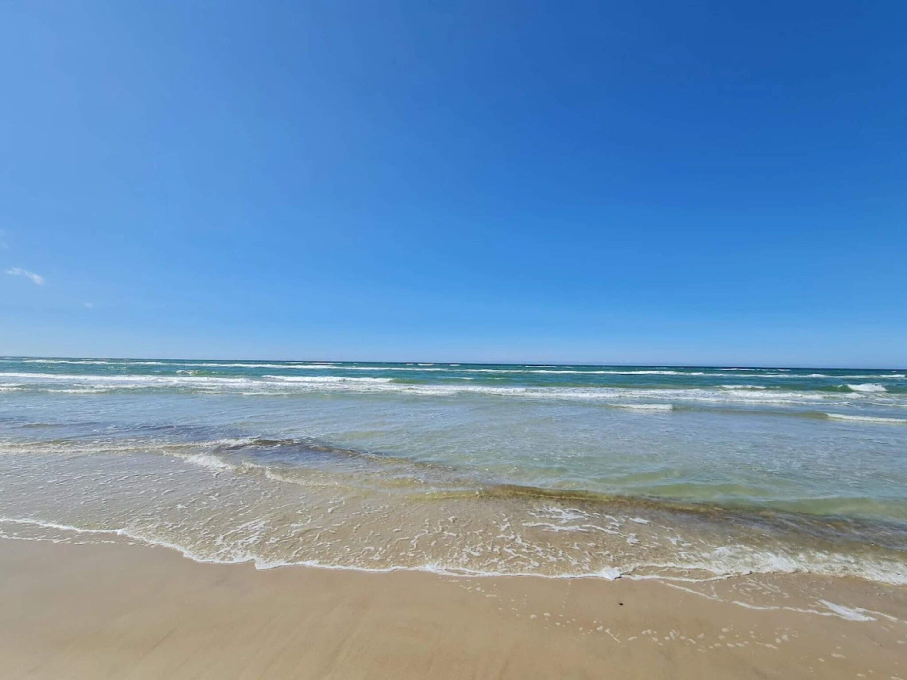 A beach with clear blue water and a sandy shore.