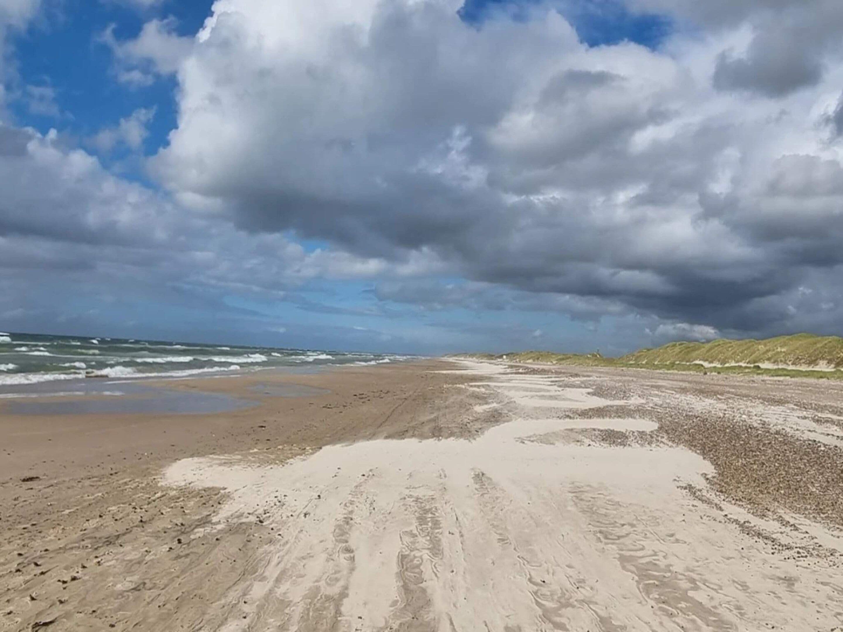 Una playa con una amplia zona arenosa y una duna cubierta de hierba al fondo.