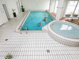 Una piscina interior con suelo de baldosas, un jacuzzi y plantas en macetas.