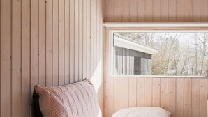 A wooden cabin room with a bed, a window, and a view of a wooden structure outside. - 6 Person Holiday Home in Gilleleje (Gilleleje)