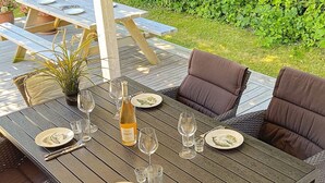 A wooden deck with a dining table set for four, surrounded by wicker chairs. - 6 Person Holiday Home in Gilleleje (Gilleleje)