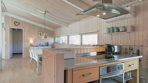 A modern kitchen with wooden paneling, a central island, stainless steel appliances, and a view to the dining area. - 6 Person Holiday Home in Gilleleje (Gilleleje)