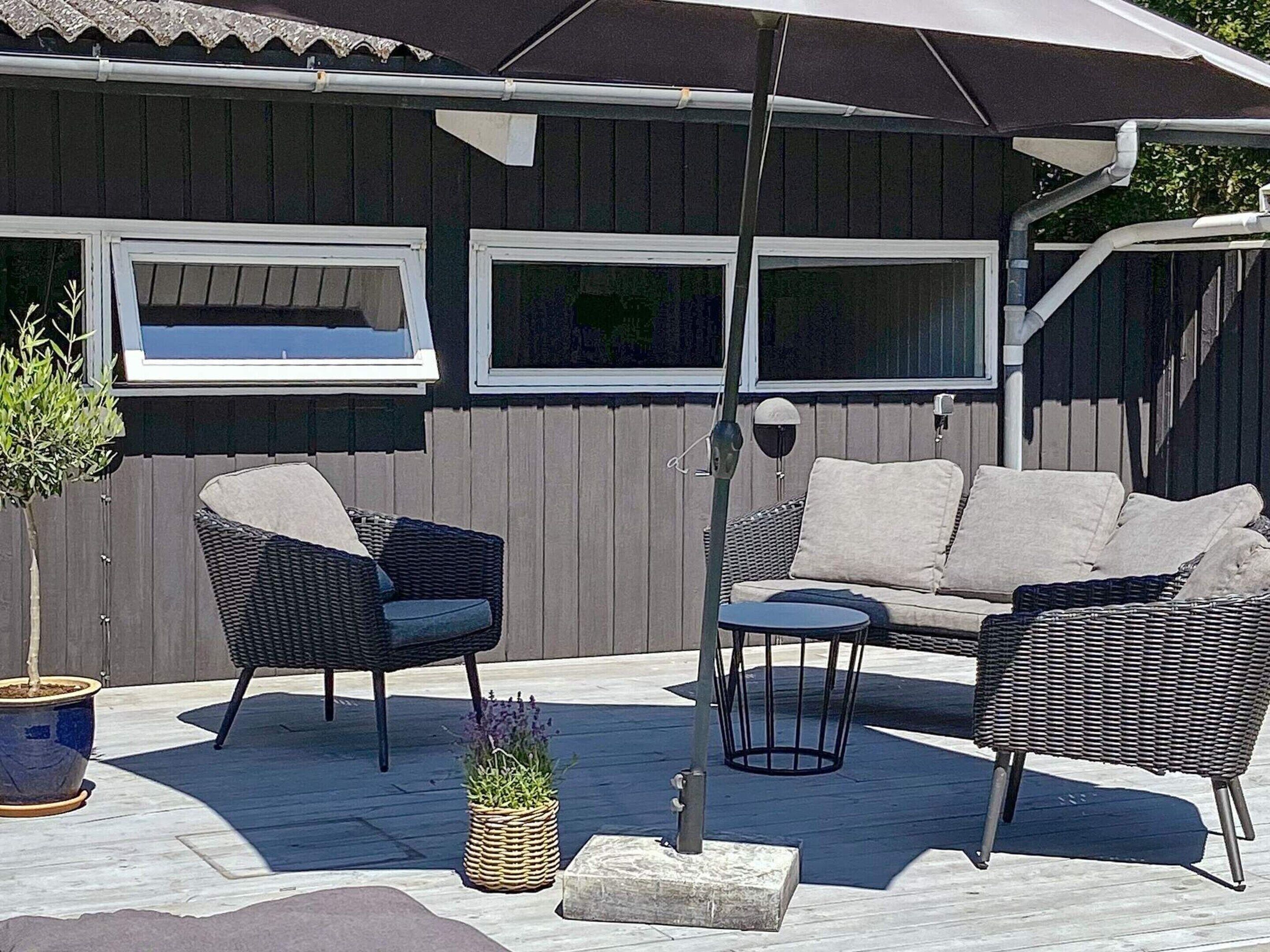 Een terras buiten met rieten meubilair, een potplant en een grote parasol.