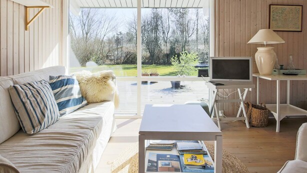 A cozy room with a white sofa, a small table with books, a TV, and a lamp. - 6 Person Holiday Home in Gilleleje (Gilleleje)