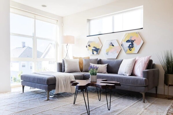 A modern living room with a grey sofa, a coffee table, and a large window providing a view of the outside.