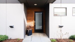 Ein moderner Hauseingang mit einer Holztür, einem kleinen Blumentopf und zwei Wandleuchten.