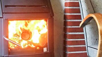 A wood-burning stove with visible flames, a brick wall, and a chair.