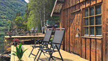 Una terraza de madera con mobiliario exterior, vista a un lago y un tractor al fondo.