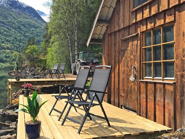 A wooden deck with outdoor seating, a view of a lake, and a tractor in the background. - 3 Person Holiday Home in Stryn (Stryn)