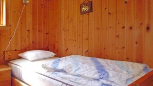 Et trægulvs værelse med en enkeltseng, et natbord og en lampe monteret på væggen.