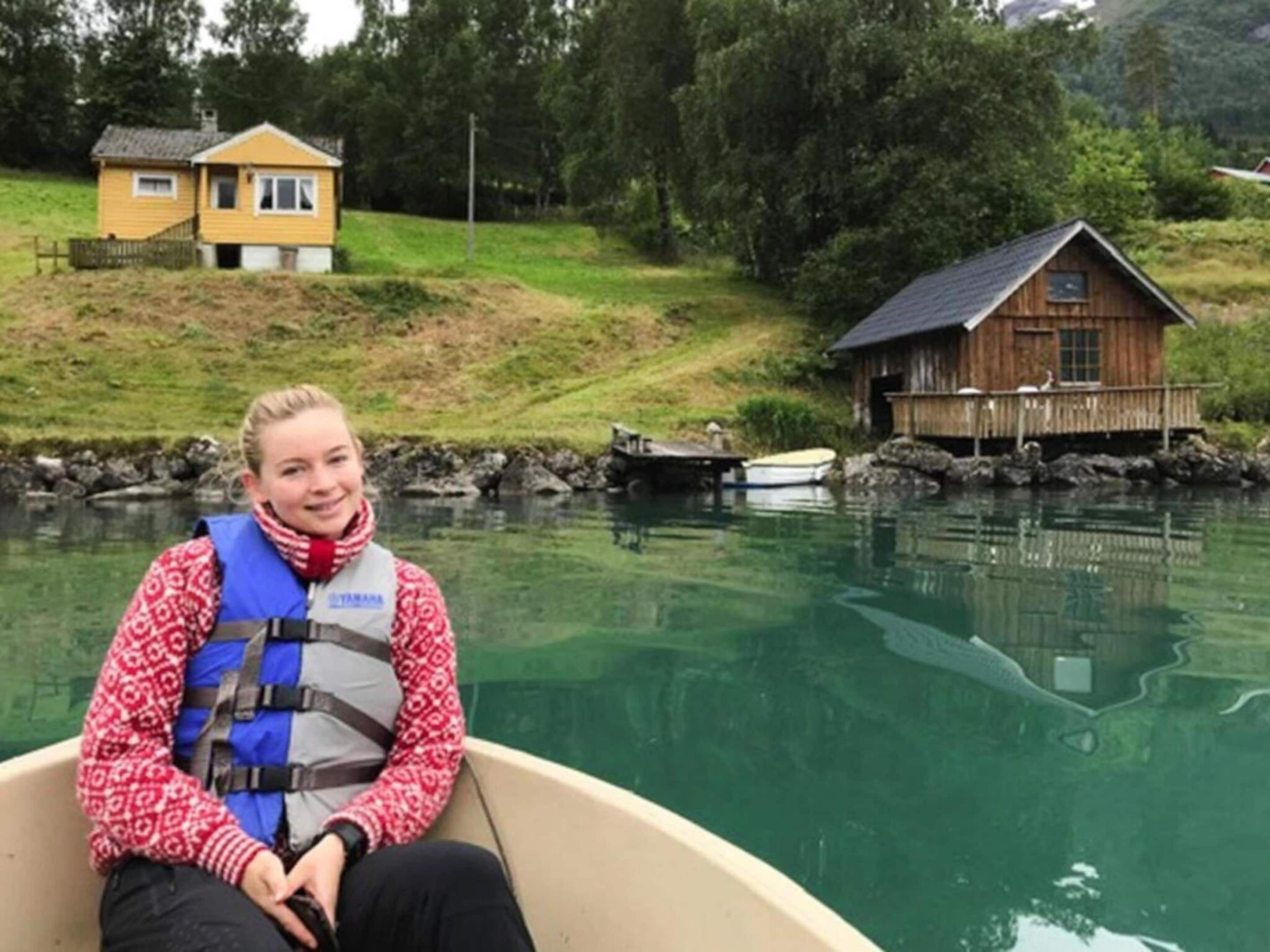 Eine Person in einem Boot in der Nähe einer Holzjagd und eines gelben Hauses an einem ruhigen See.