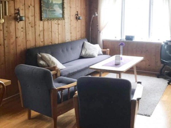 A room with a wooden paneled wall, a grey sofa, a small table, and a chair. - 3 Person Holiday Home in Stryn (Stryn)