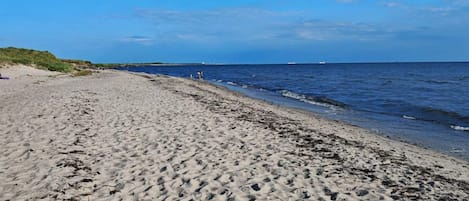 A sandy beach with gentle waves, a clear sky, and distant boats.