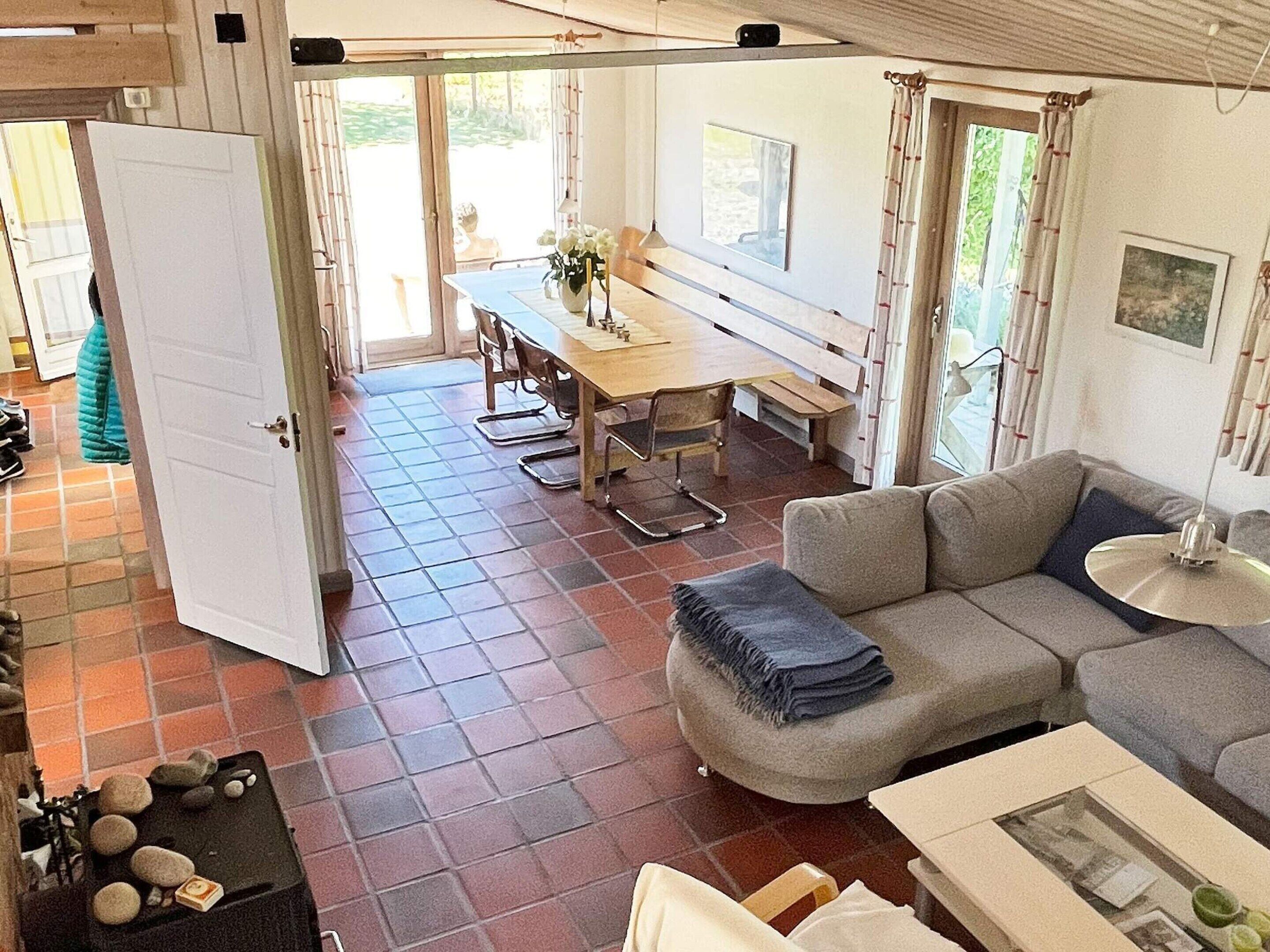 A spacious living area with a sofa, a dining table with chairs, and a view of the outdoors through large windows.