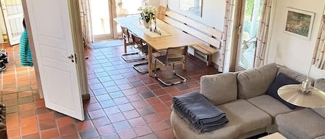 A spacious living area with a sofa, a dining table with chairs, and a view of the outdoors through large windows.