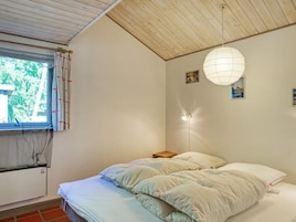 Un dormitorio con cama, ventana con cortinas, lámpara de pared y mesita de noche.