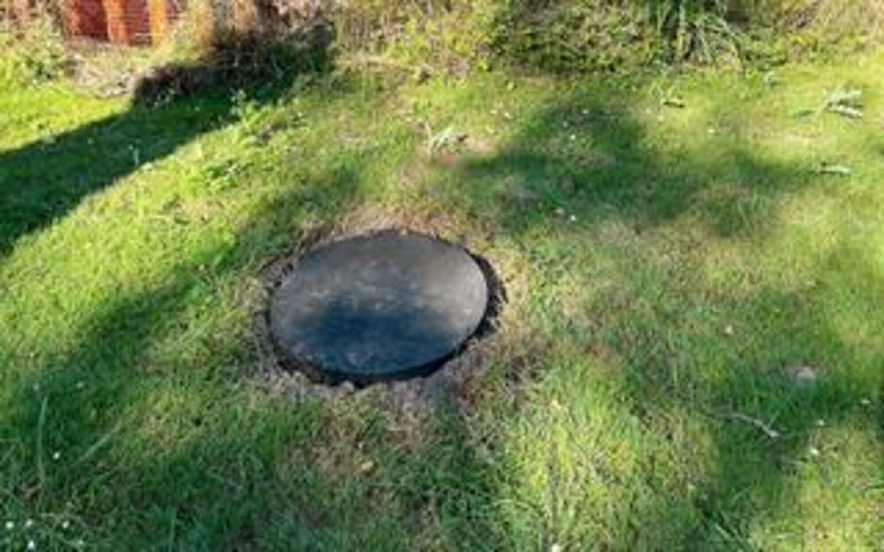 A circular hole in the ground surrounded by grass.
