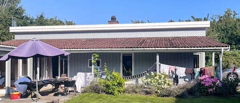 A two-story house with a covered porch, a barbecue area, and a garden with flowers.