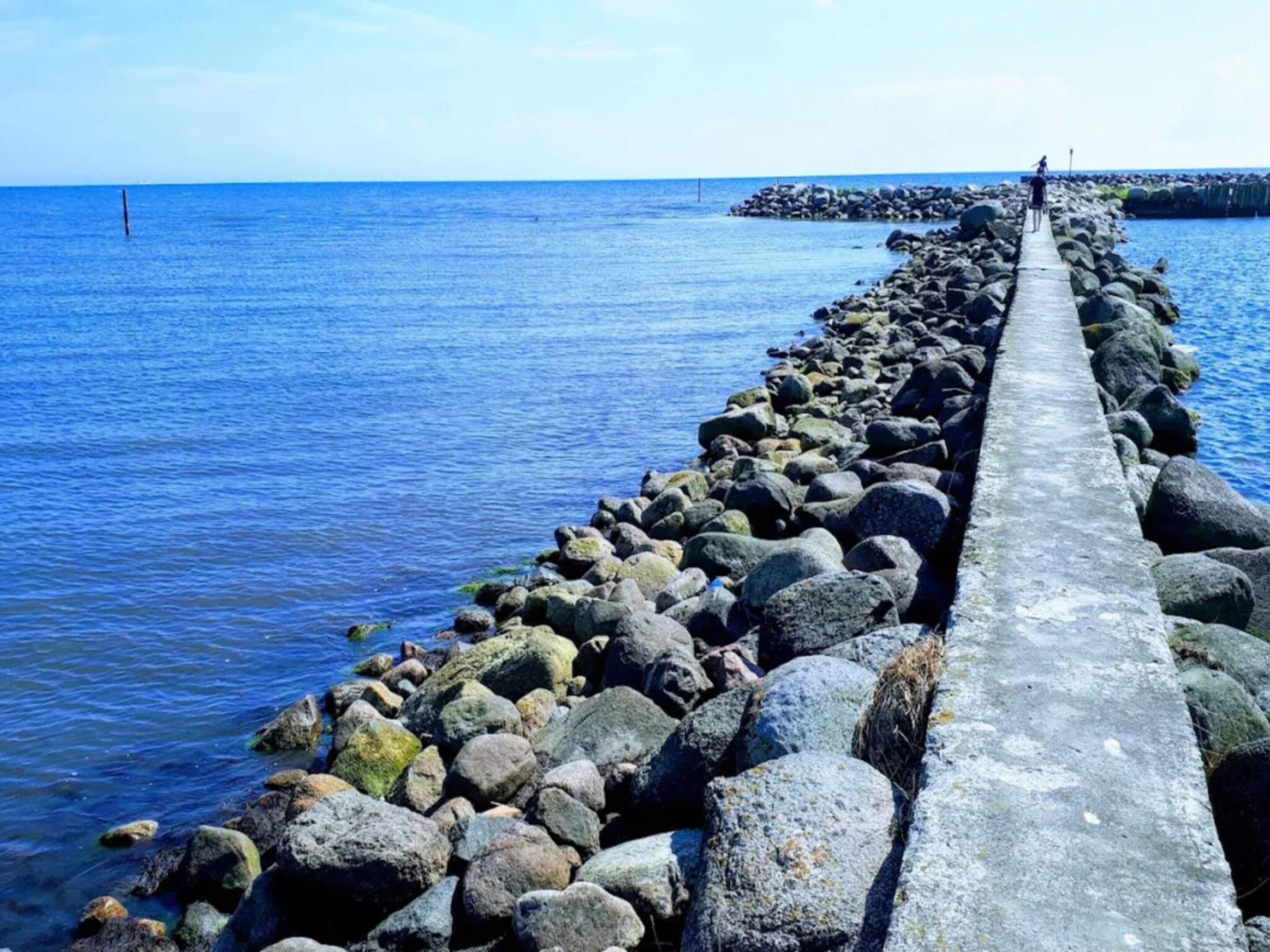 A concrete pier extending into a body of water, surrounded by large rocks.