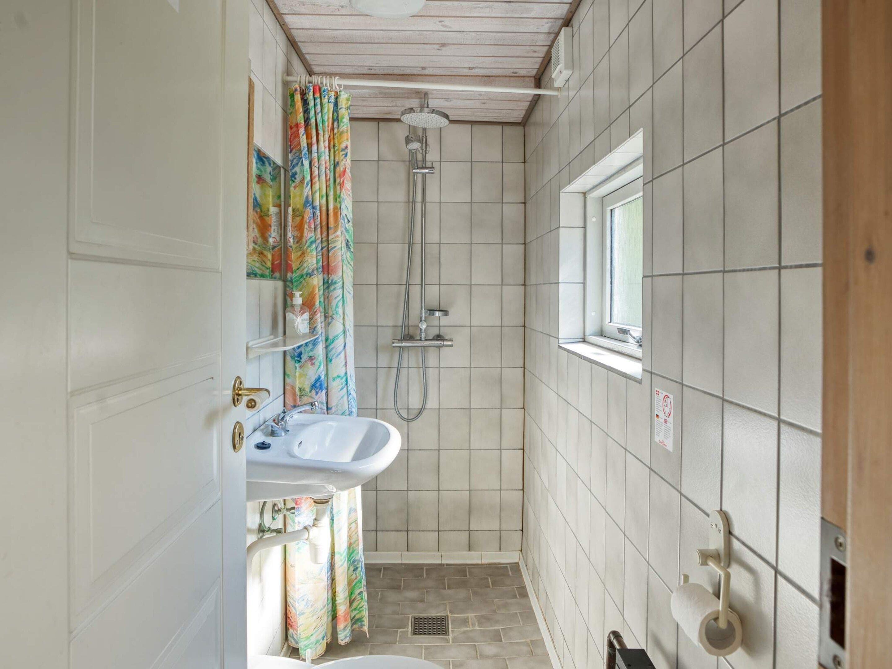 A bathroom with a shower, a sink, and a window.