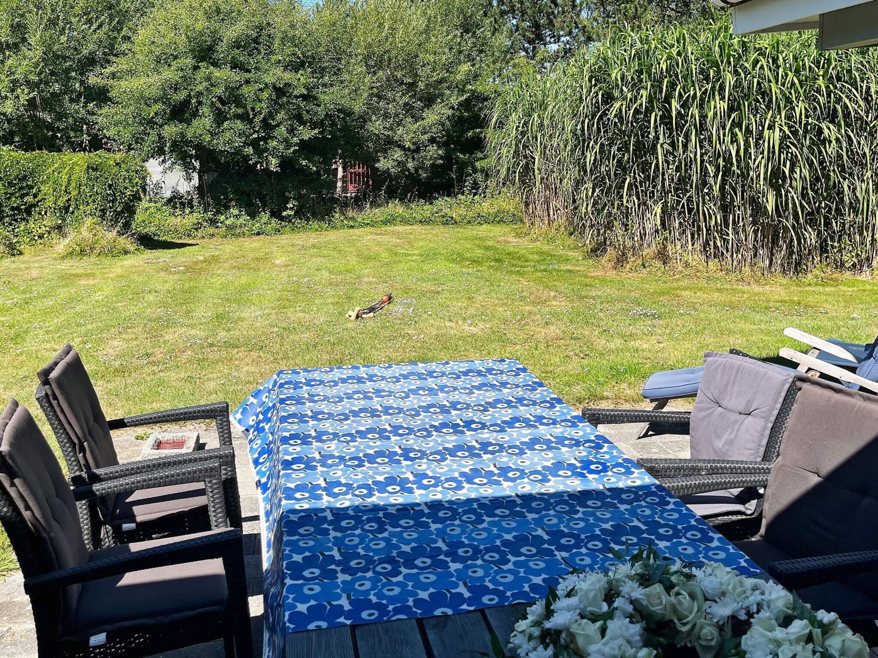 Eine Außenpatio mit einem Tisch, bedeckt mit einer blau gemusterten Tischdecke, umgeben von Korbstühlen.