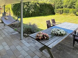 Un patio exterior con mesa de madera, sillas y una hamaca.