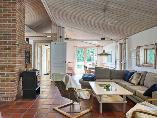 A spacious living area with a fireplace, a sofa, a dining table, and a view of the outdoors. - 10 Person Holiday Home in Dannemare (Dannemare)