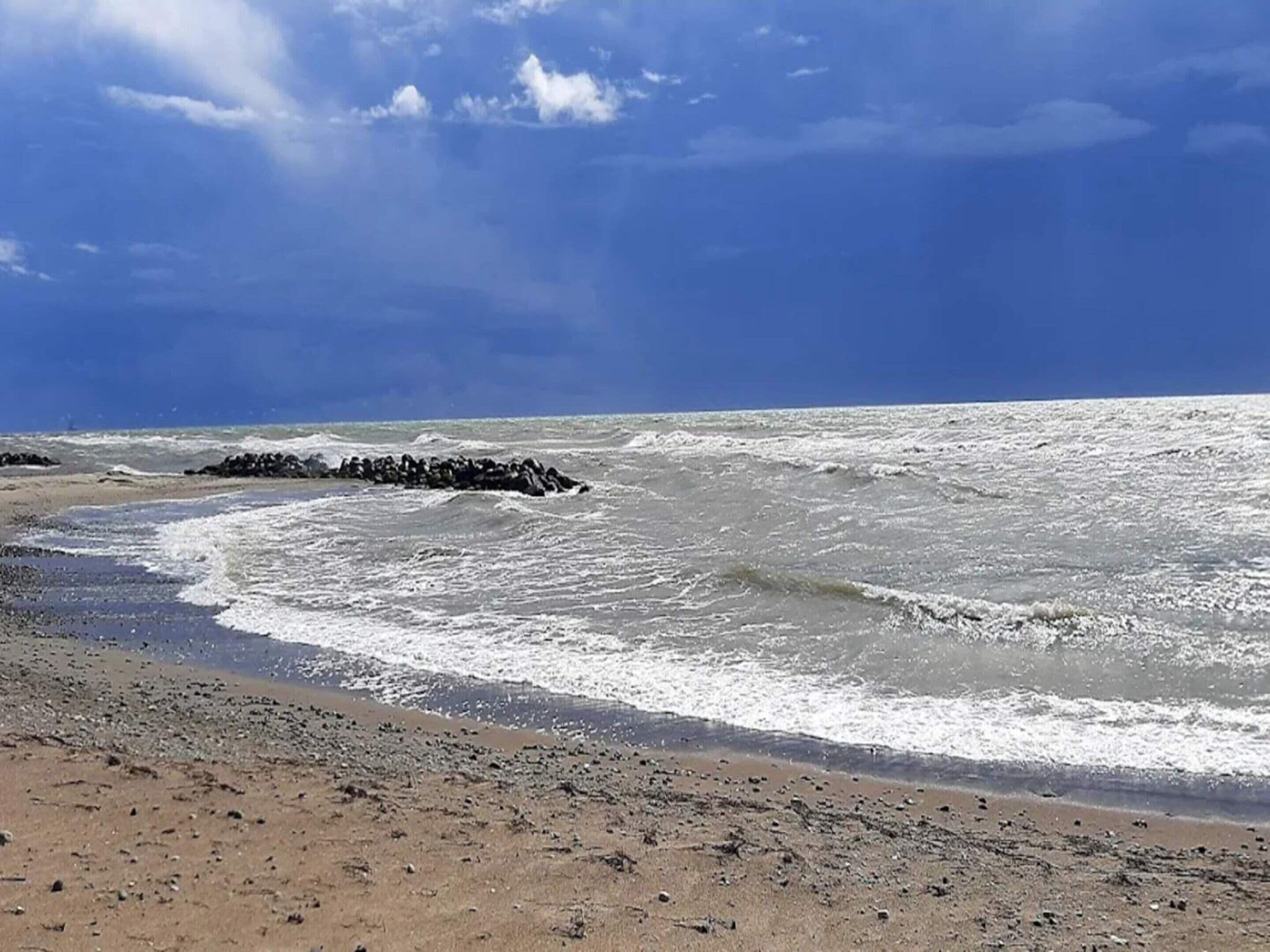 Ein Strand mit Wellen, blauem Himmel und einem Felsen.