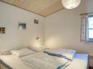 A bedroom with a wooden ceiling, a bed with white bedding, a wall-mounted lamp, and a window with curtains. - 10 Person Holiday Home in Dannemare (Dannemare)