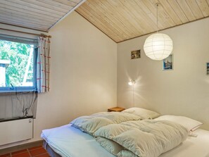 A bedroom with a bed, a window with curtains, a wall-mounted light, and a small bedside table. - 10 Person Holiday Home in Dannemare (Dannemare)