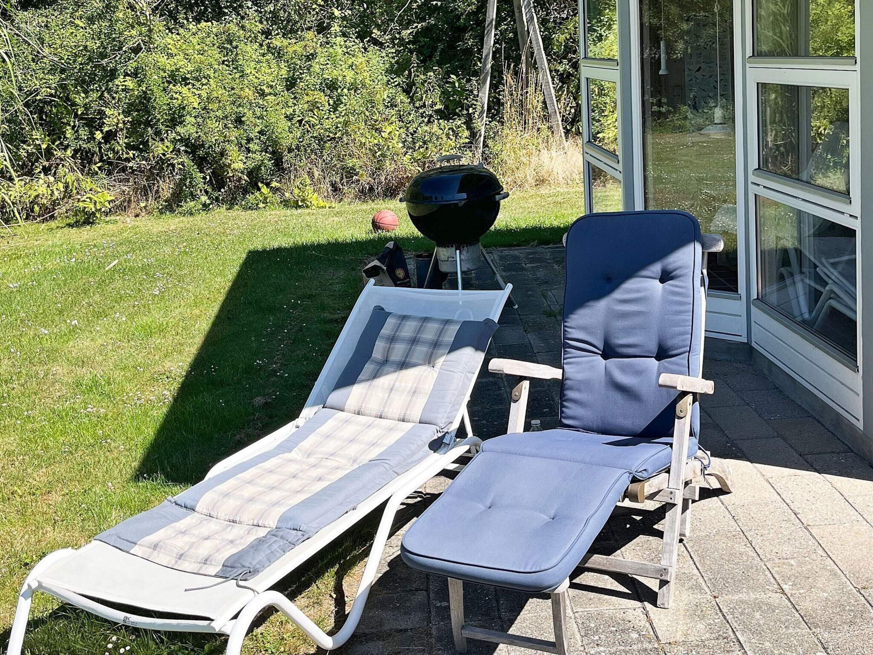 Zwei Liegestühle mit Kissen, ein Grill und eine Glastür, die in einen Garten führt.