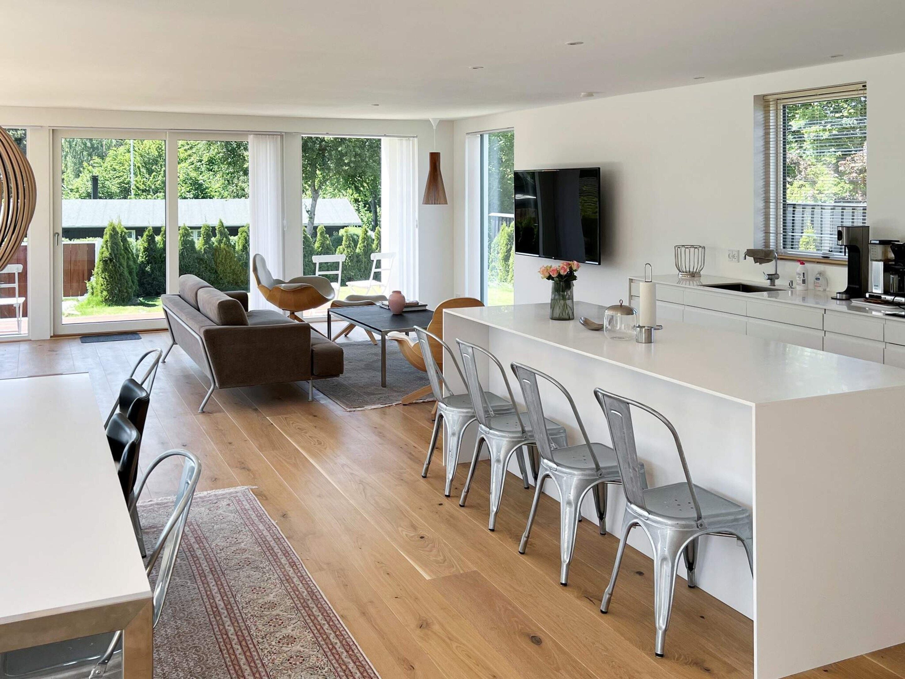 Una cocina moderna con una isla central, comedor con sillas y un amplio ventanal con vistas al exterior.