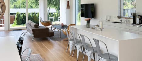 Una cocina moderna con una isla central, comedor con sillas y un amplio ventanal con vistas al exterior.