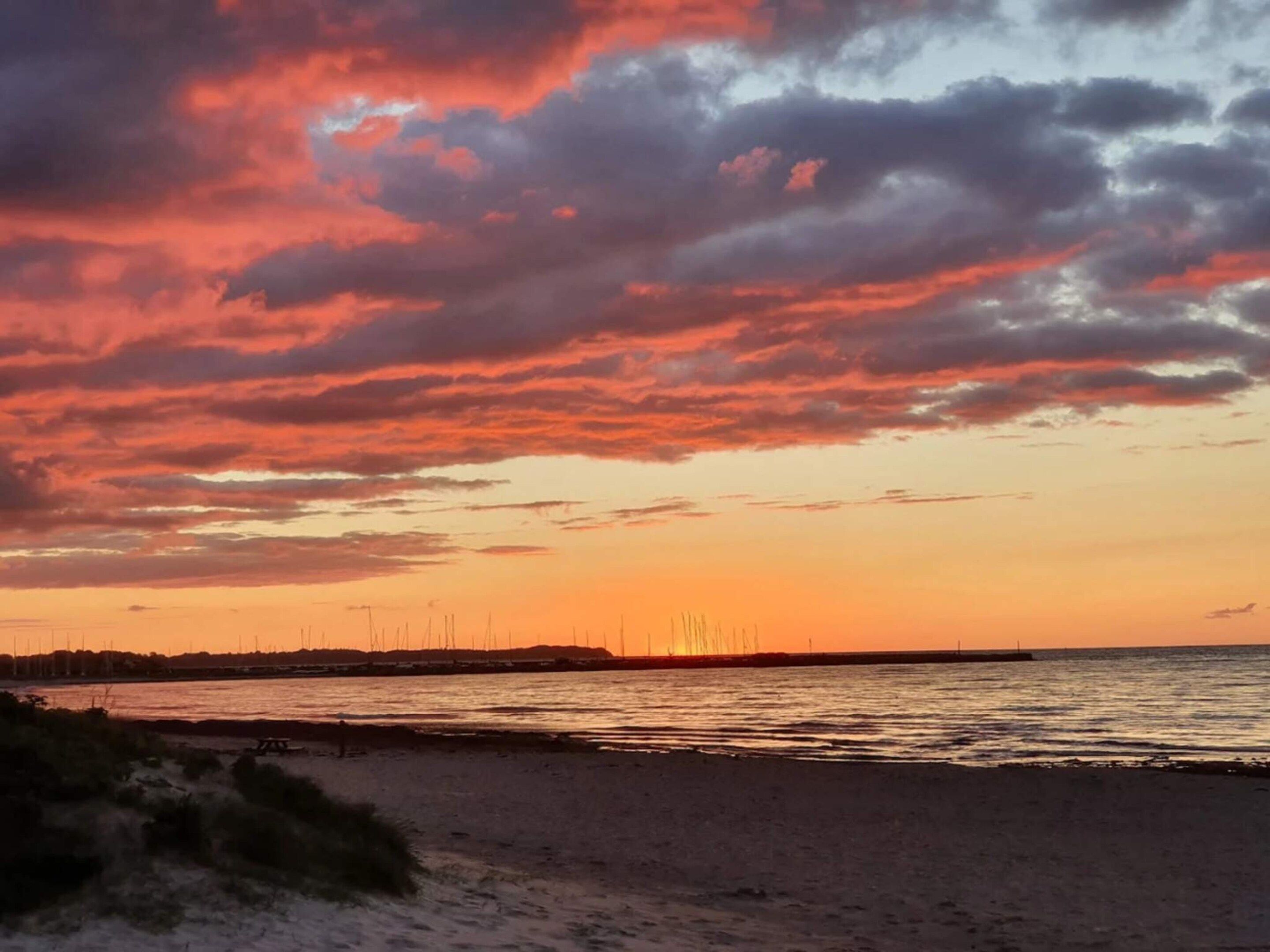 Una playa con un atardecer, agua tranquila y una costa distante con construcciones.
