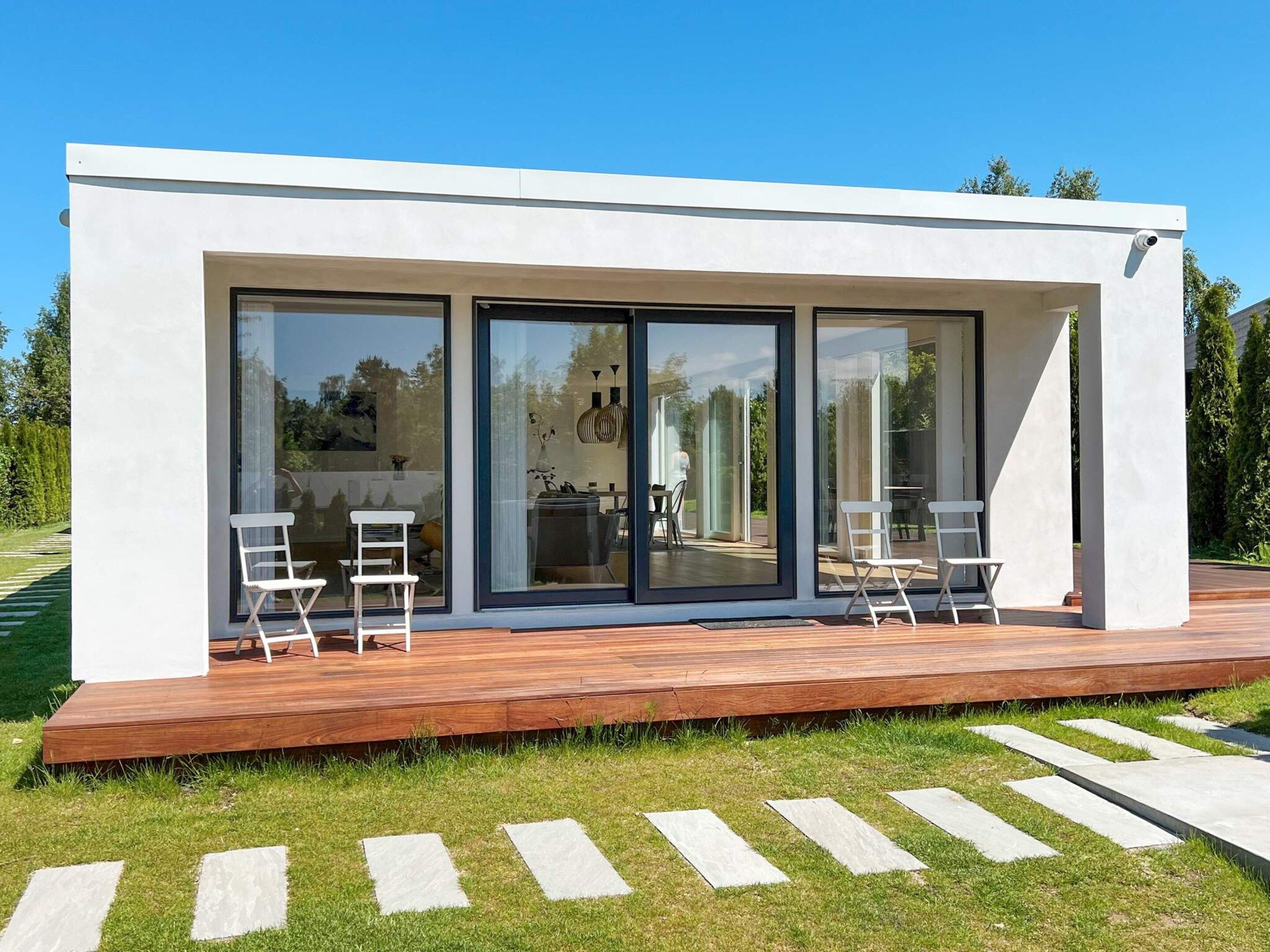 A modern house with large glass windows, a wooden deck, and outdoor seating.